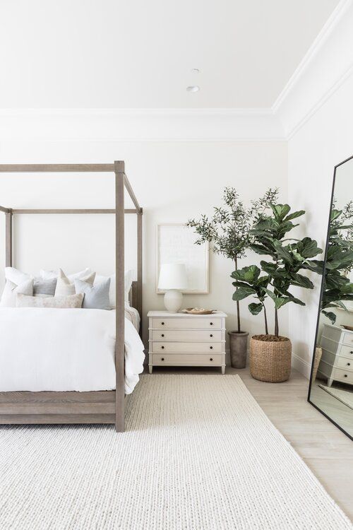 a neutral modern bedroom with a wooden bed, statement plants, an oversized mirror and white nightstands