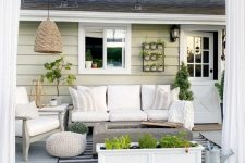 a neutral modern farmhouse terrace with white upholstered furniture, a fire pit, potted greenery, a pendant lamp and neutral textiles