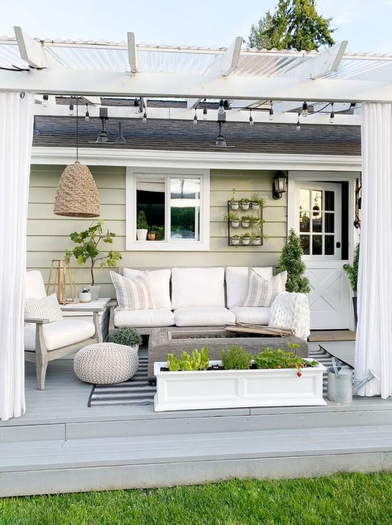 a neutral modern farmhouse terrace with white upholstered furniture, a fire pit, potted greenery, a pendant lamp and neutral textiles