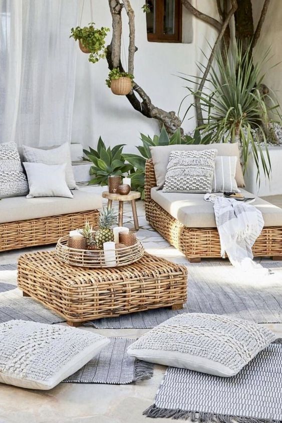 a neutral modern terrace with wicker furniture and neutral upholstery, lots of greenery and succulents around, cushions and layered rugs