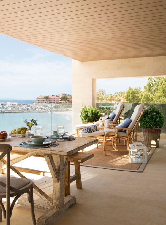 a neutral rustic coastal terrace with shabby chic wooden furniture, white loungers with blue pillows, potted greenery