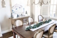 a neutral shabby chic dining room with an elegant inlay console, a dark stained table and chic chairs, a crystal chandelier