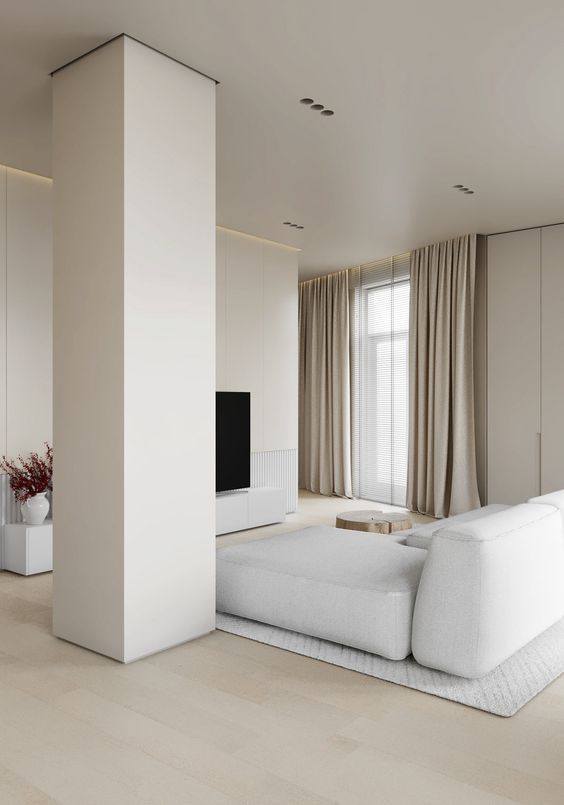 a neutral ultra minimalist living room with a TV, a white sectional, a pillar and neutral textiles