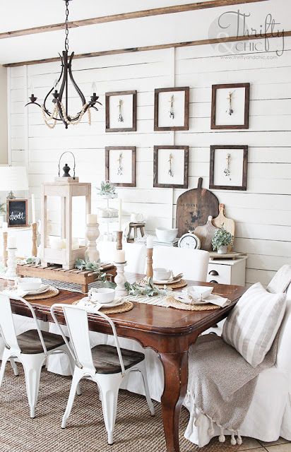 a neutral vintage farmhouse dining room with planked walls, a dark stained table, white chairs and upholstered loveseats