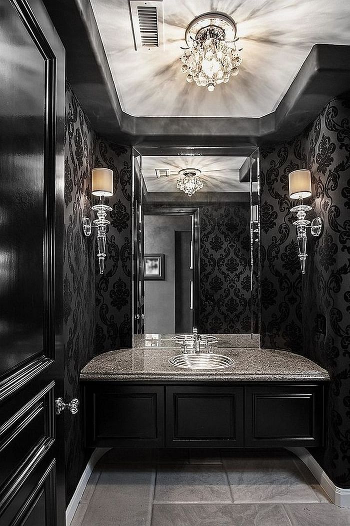 a refined Gothic bathroom with printed wallpaper, chic black furniture, a large mirror and cool crystal lamps and a chandelier