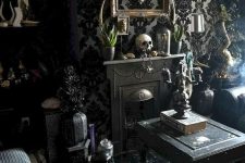 a refined Gothic living room with catchy wallpaper, skulls, black furniture, a mini fireplace, some greenery and exquisite touches