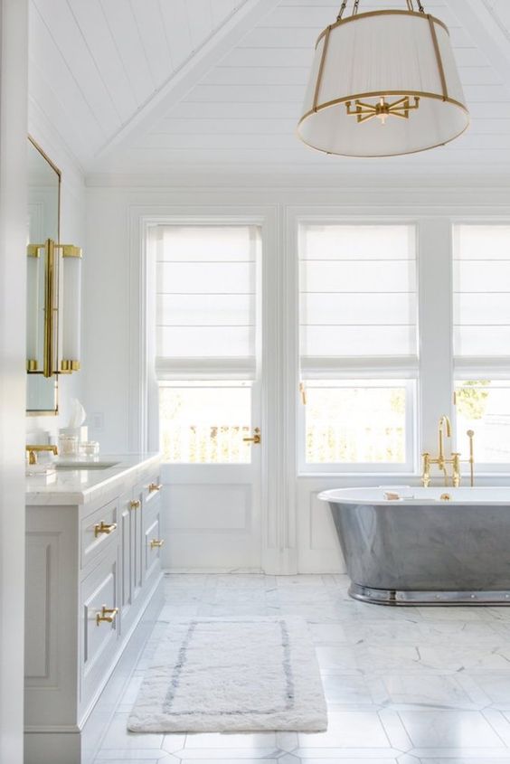 a refined coastal bathroom with a marble floor, a metal clad tub, a large vanity and gold touches and fixtures