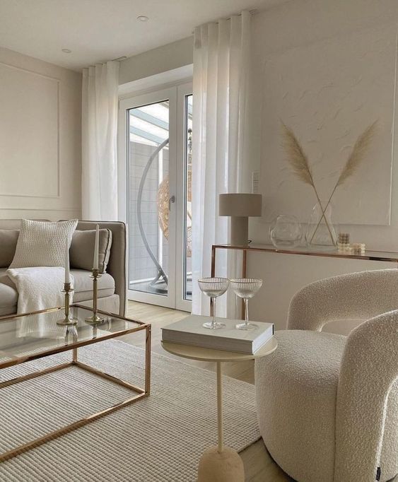 a refined contemporary living room with paneling, a glass console table, neutral furniture, a duo of side tables and neutral textiles