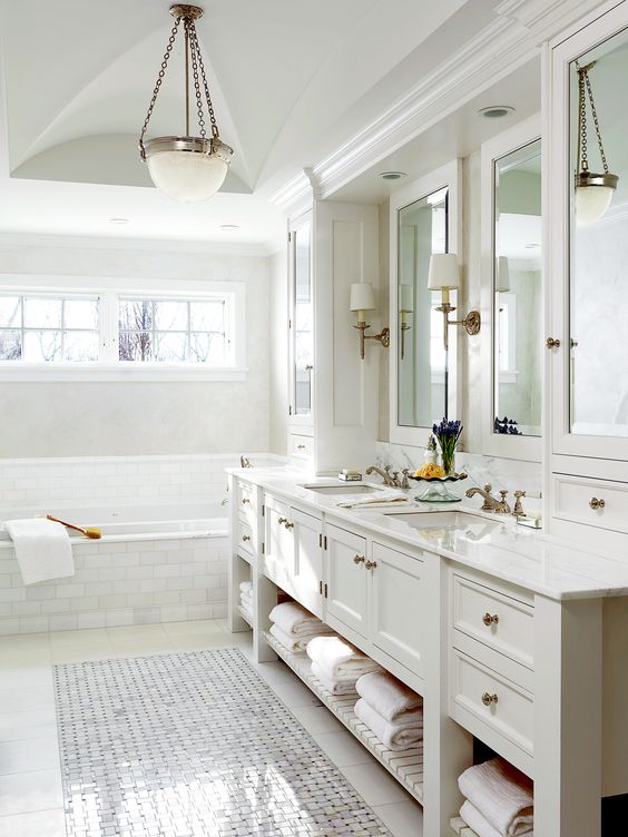 a refined neutral bathroom with a vintage built-in vanity, a tub clad with marble tiles, a pendant lamp and mirrors