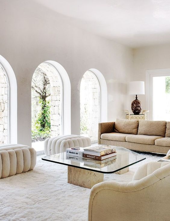 a refined neutral living room with warm-colored seating furniture, a glass and stone coffee table and a chic lamp in the corner