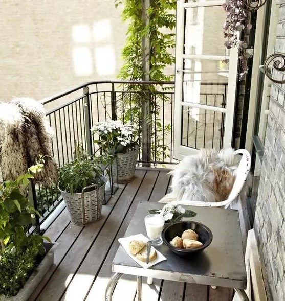 a relaxed Scandinavian balcony with white metal chairs and a metal table, potted greenery and blooms, faux fur covers is cool