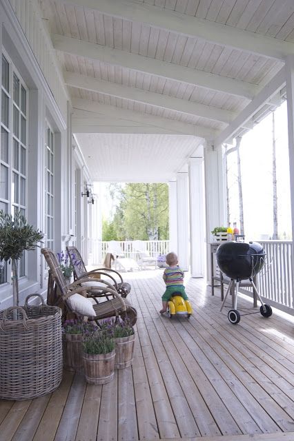 a relaxed Scandinavian porch with rattan chairs and potted plants and blooms and white loungers placed in the sunshine spot