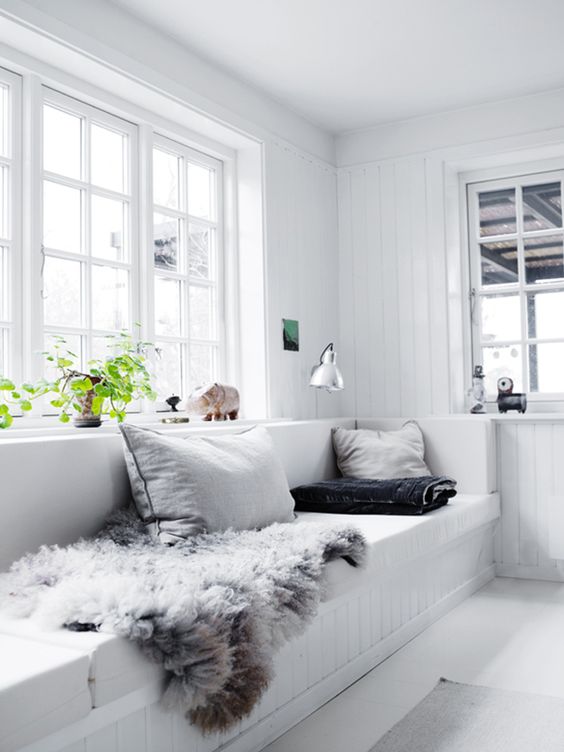 a relaxed white Scandinavian sunroom with a built in sofa, neutral pillows, a sconce and a potted plant is all cool