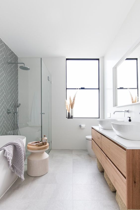 a serene contemporary bathroom with an oval tub, a floating vanity, a grey herringbone accent wall and a wooden side table