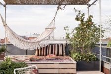 a simple boho rofotop terrace with a raised platform bed, a hammock, a woven chair, printed textiles and potted plants around