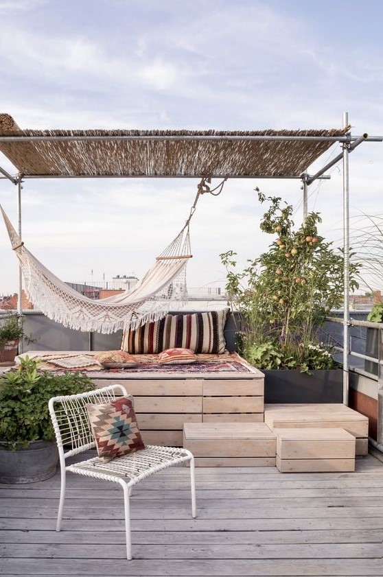 a simple boho rofotop terrace with a raised platform bed, a hammock, a woven chair, printed textiles and potted plants around