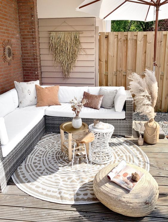 a simple neutral boho terrace with a wicker corner sofa, an arrangement of coffee tables, a dried grass hanging and an umbrella