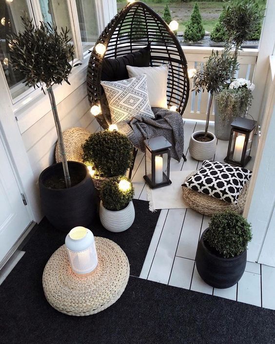 a small Scandinavian balcony with a black egg-shaped chair, candle lanterns and string lights, potted greenery