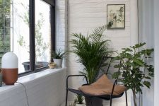 a small Scandinavian sunroom with white planked walls and a floor, with a glass ceiling, a black metal chair and some potted plants