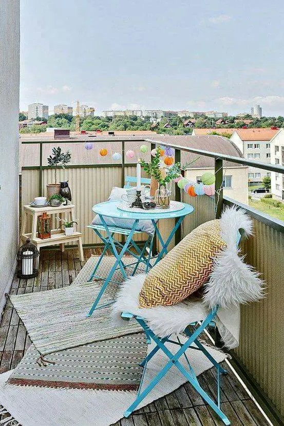 a small and colorful balcony with bright blue furniture, a ladder, candle lanterns and rugs