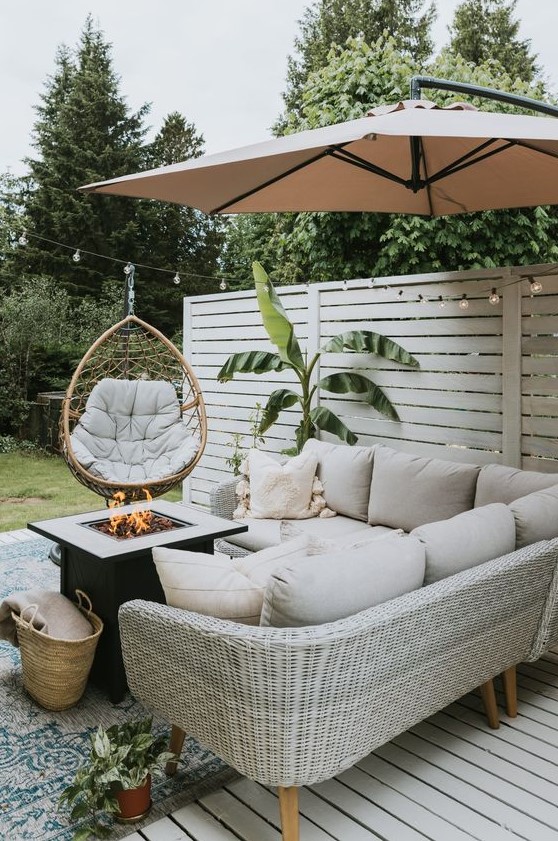 a small and cool farmhouse patio with a neutral wicker corner sofa, a fire pit, a pendant egg chair and a potted plant