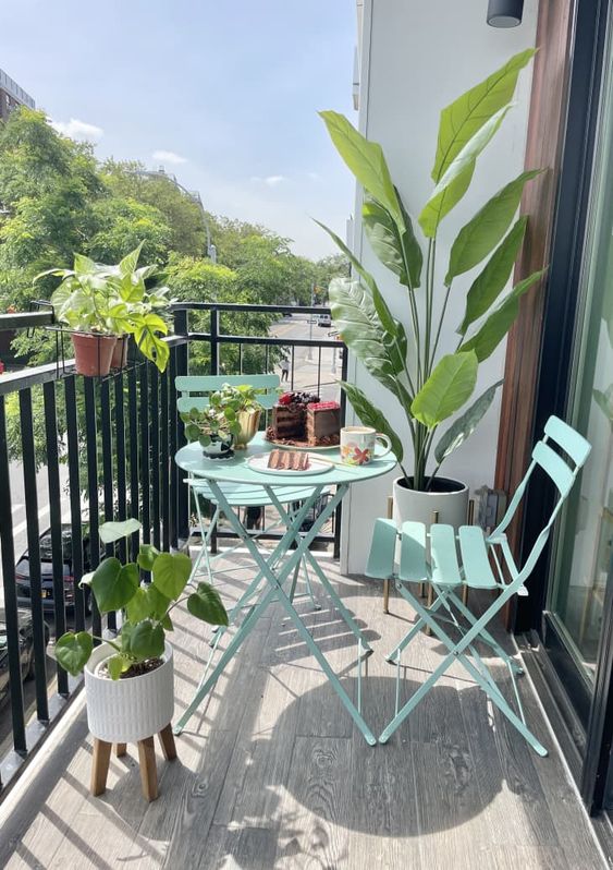 a small and stylish balcony with mint blue folding furniture, potted blooms and plants and a cool view