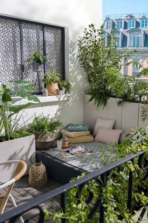 a small balcony with a daybed and bright pillows, potted greenery and a chair and some baskets is cool