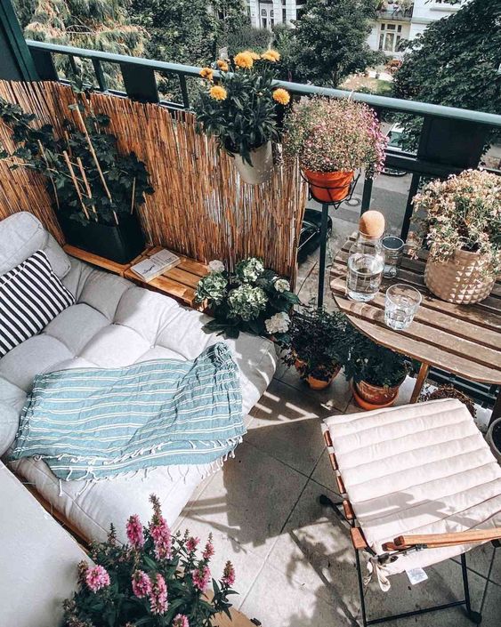 a small balcony with a daybed, folding table and chair, potted blooms and greenery is a welcoming space
