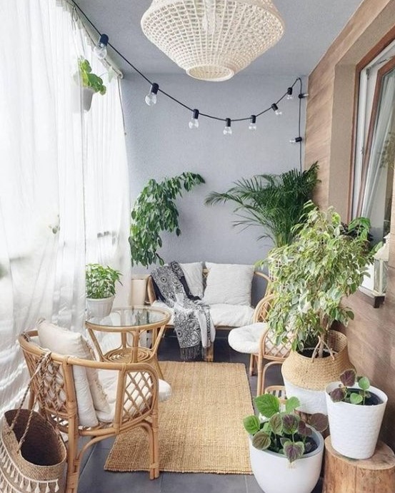 a small balcony with sheer curtains, lights, a wicker lamp, rattan furniture, statement plants and baskets is very cozy