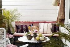 a small boho chic terrace with a bench and a chair, boho textiles and pillows plus some potted greenery