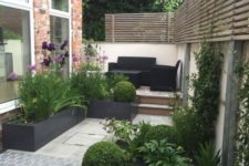 a small contemporary terrace with dark furniture, potted greenery and blooms and wooden screens for privacy