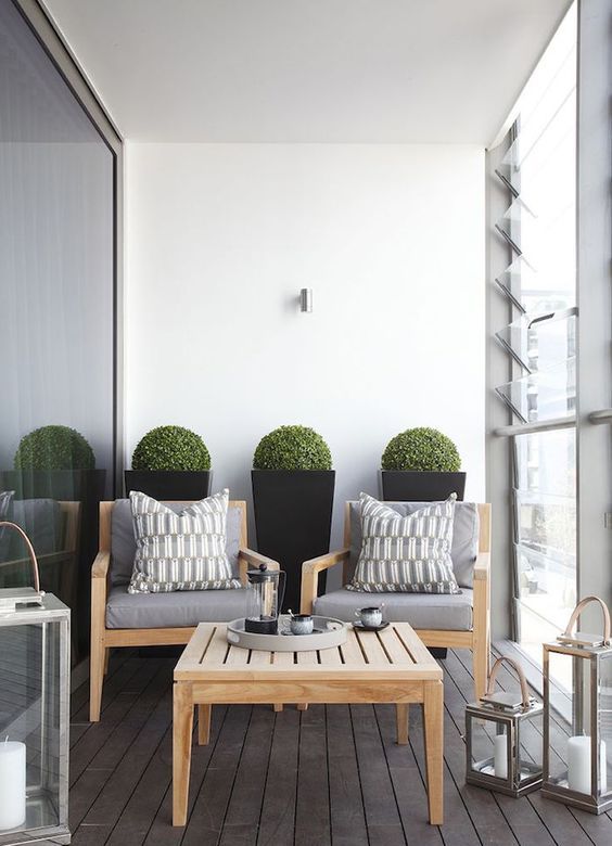 a small contemporary terrace with simple wooden furniture, large candle lanterns and potted boxwood