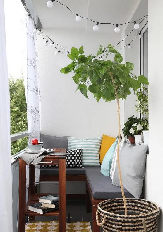 a small cozy balcony with an L-shaped upholstered bench, a small coffee table and potted plants