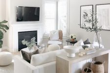 a small neutral living space with a white sofa and chairs, a built-in fireplace, a console and some accessories and greenery to refresh the space