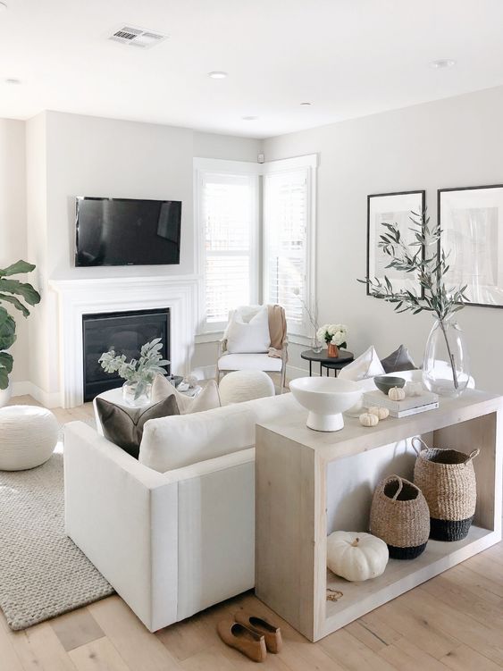 a small neutral living space with a white sofa and chairs, a built-in fireplace, a console and some accessories and greenery to refresh the space
