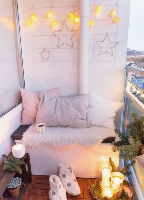 a small winter balcony with lots of lights, star decor, faux fur, pastel pillows, candles, pinecones and evergreens