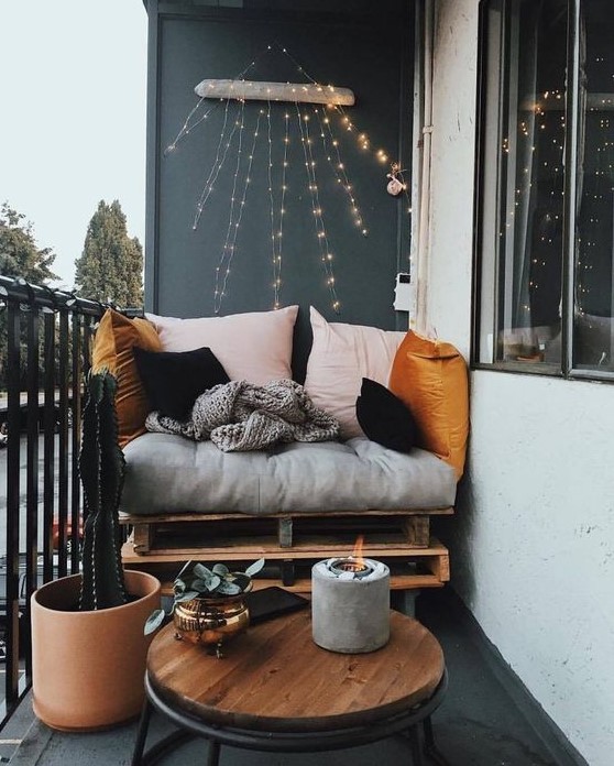 a small yet chic balcony with a pallet seat, colorful pillows, a table, a cactus and a candle in a concrete candleholder