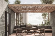 a soothing contemporary terrace with a built-in bnehc with grey cushions, rattan chairs with grey upholstery, loungers and low coffee tables