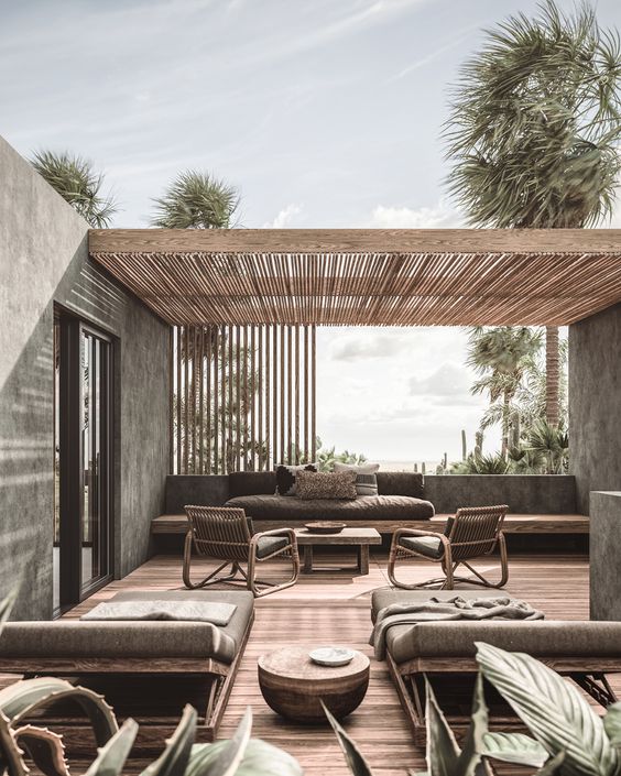 a soothing contemporary terrace with a built-in bnehc with grey cushions, rattan chairs with grey upholstery, loungers and low coffee tables