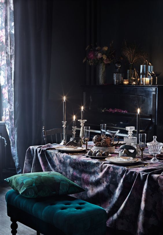 a sophisticated dining room with black walls, a black piano, vintage chairs, an emerald bench, candles and floral linens