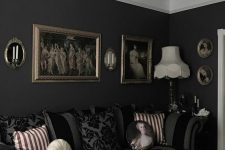 a stylish Gothic living room with black walls, a striped sofa, artworks, a chandelier and printed pillows
