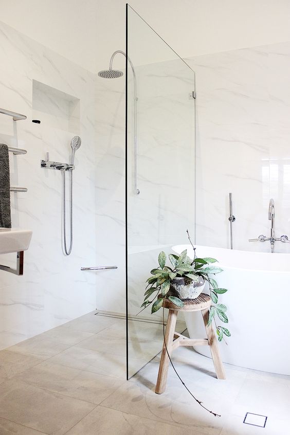 a stylish neutral bathroom with marble and tan tiles, an oval tub, a wooden stool and a potted plant in a stone planter