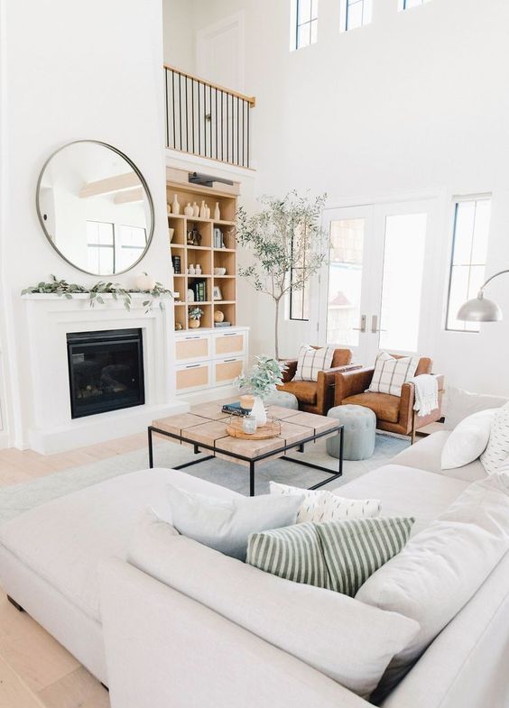 a stylish neutral living room with a uilt-in fireplace, a white sectional, brown leather chairs and a catchy table