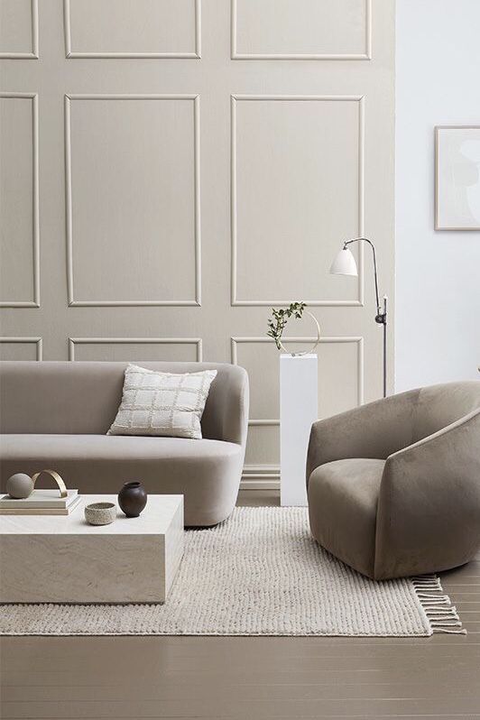 a stylish neutral living room with wainscoting, a taupe sofa and chair, a neutral stone slab coffee table and neutral textiles is chic