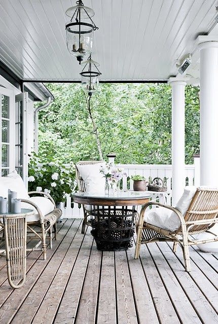 a summer Scandinavian porch with rattan furniture, a round wooden table, potted plants and blooms and hanging lights