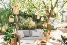 a summer boho patio with a grey sofa, neutral chairs, a low coffee table, lanterns hanging over the space, potted plants