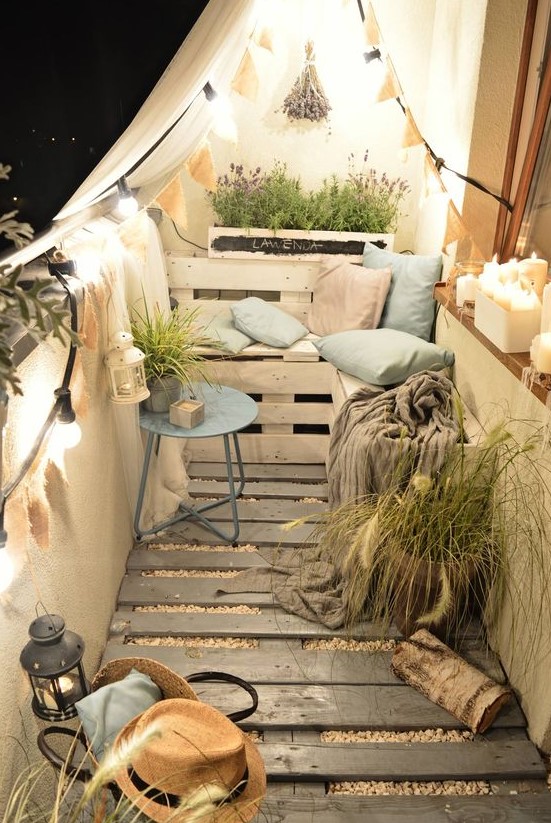 a tiny cozy balcony with a wooden floor, pallet furniture and pots, potted greenery and blooms and lights and candles