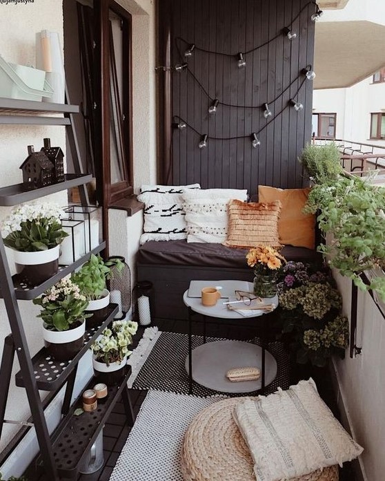 a tiny monochromatic balcony with black and white walls, blakc furniture, potted greenery and blooms and various pillows and rugs