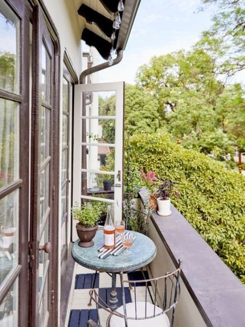 a tiny narrow balcony with a round table and a couple of chairs, potted blooms and greenery is small yet comfy