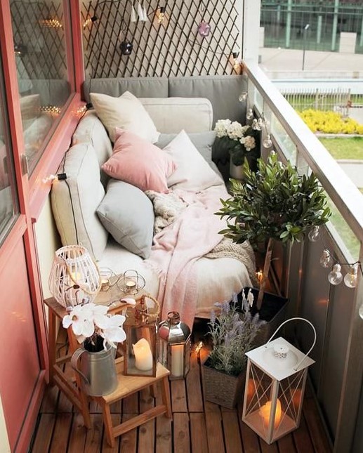 a tiny narrow balcony with pastel textiles and pillows, potted greenery and blooms, candle lanterns and wooden furniture